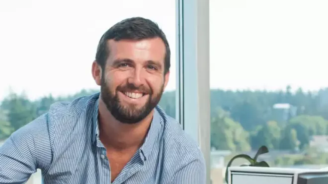 Colin smiling in front of a window with trees in the background